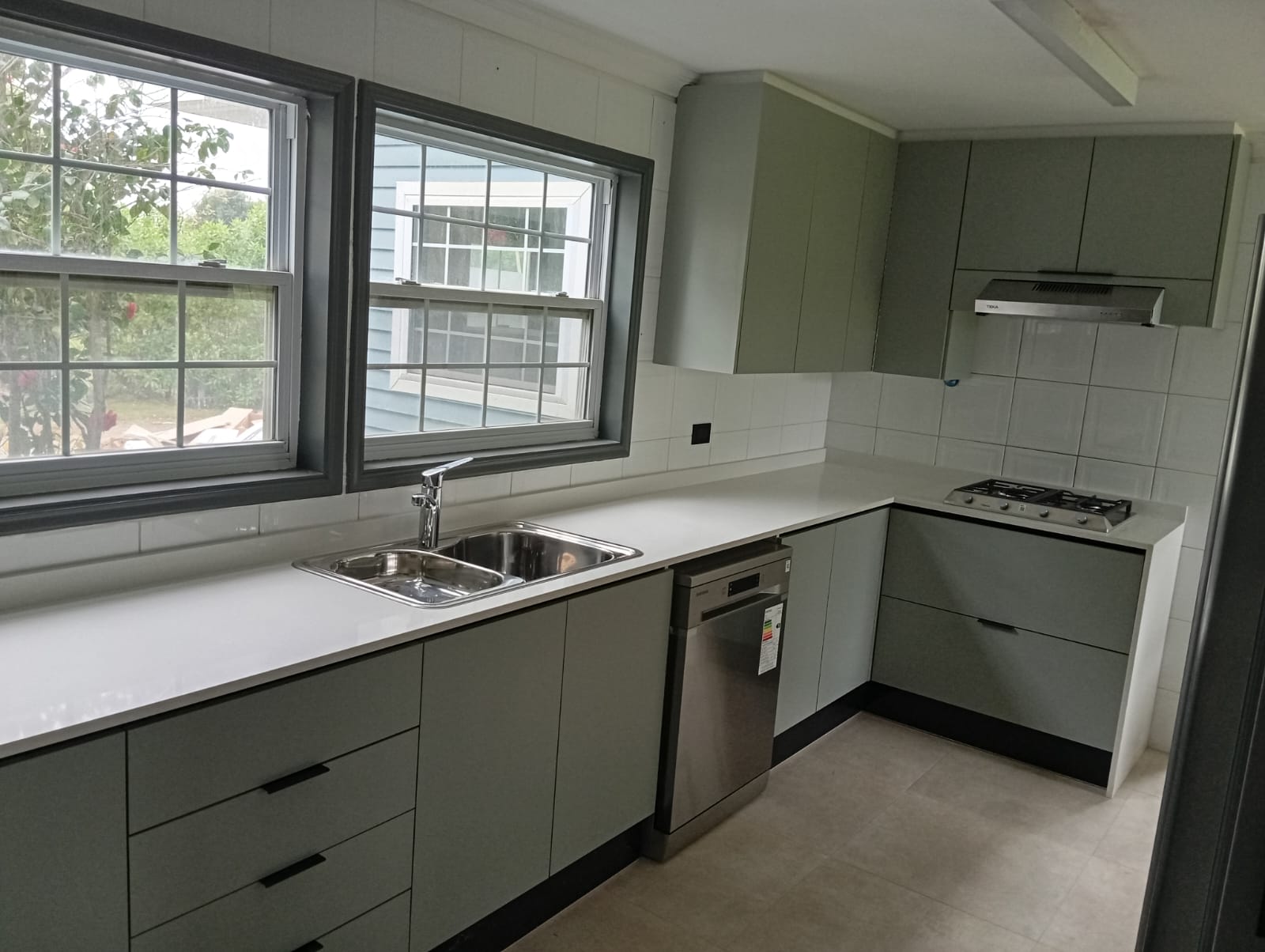 Cocina remodelada con muebles verde salvia, cubierta blanca y ventanas al jardín